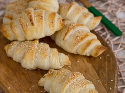 Goldbraune, mit Sesam bestreute Frischkäse-Hörnchen sind auf einem Holzbrett angeordnet.