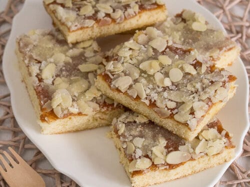 Mehrere Stücke Blitz-Butterkuchen, belegt mit gehobelten Mandeln, sind auf einem weißen ovalen Teller angeordnet.