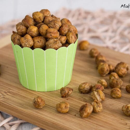 Gesunder Kichererbsen Snack 3 Gebackene Kichererbsenauf einem Holzbrett, mit zusätzlichen Kichererbsen in der Nähe.