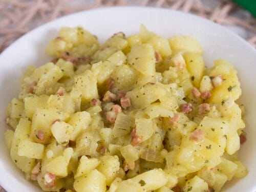 Deutscher Kartoffelsalat in einer Schüssel mit gewürfelten Kartoffeln, knusprigem Speck und Brühe.