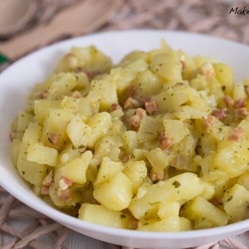 Kartoffelsalat mit Brühe und Speckstücken in einer weißen Schale.