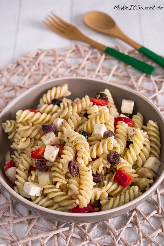 Eine Schüssel mit einem griechischen Nudelsalat, der Nudeln, Feta, Paprika und Oliven enthält. Darüber ist Oregano gestreut.