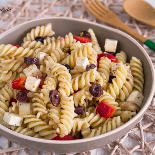 Griechischer Nudelsalat mit Fetakäse, schwarzen Oliven und roter Paprika in einer Schüssel.