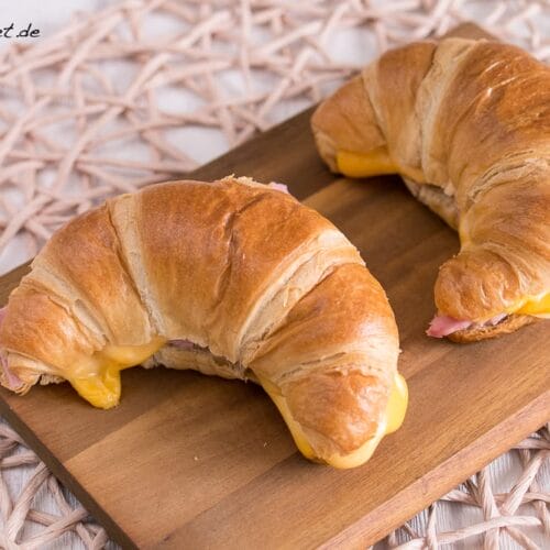 Croissant mit Schinken und Käse 3 Zwei gefüllte Croissant mit Schinken und geschmolzenem Käse auf einem Holzbrett.