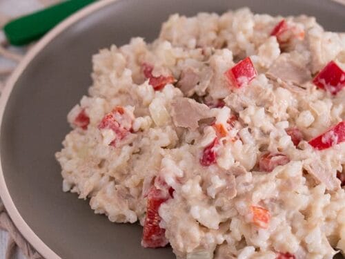Ein brauner Teller mit Reissalat mit Reis, Thunfisch, roten Paprikastücken und einem cremigen Dressing.