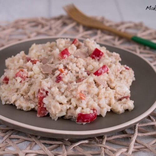 Ein Teller cremiger Reissalat mit Thunfisch, belegt mit roten Paprikastücken.