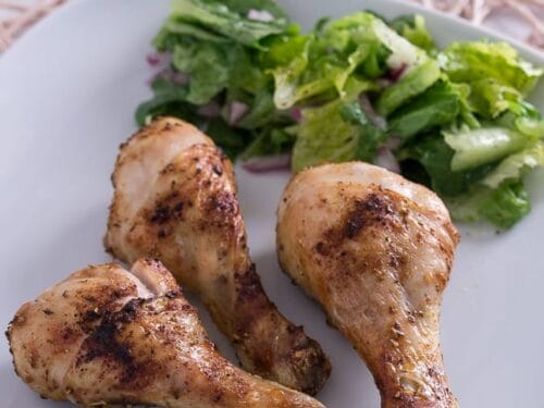 Drei knusprige Hähnchen-Unterkeulen aus der Heißluftfritteuse auf weißem Teller mit frischem grünem Salat.
