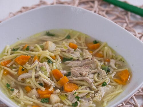 Schüssel Hühnersuppe mit sichtbaren Karotten und Petersilie.