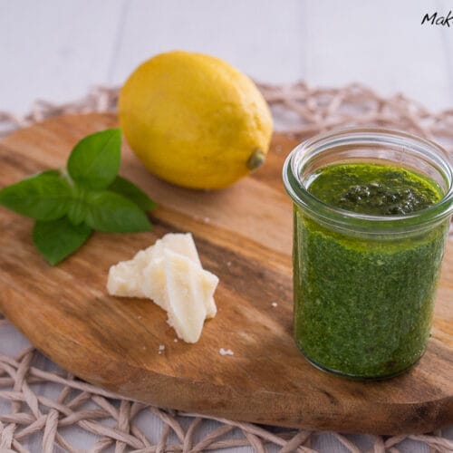 Zitronenpesto mit Basilikum 3 Zitronenpesto im Glas mit Zitrone, frischen Basilikumblättern und Parmesan auf einem Holzbrett.