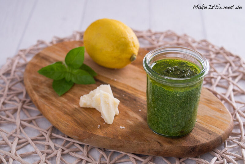 Brettchen mit einem Glas Zitronenpesto, daneben eine Zitrone, etwas Basilikum und Parmesan