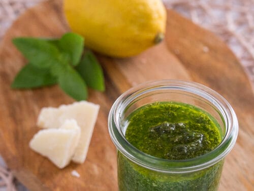 Zitronenpesto im Glas mit frischer Zitrone, Basilikumblättern und Parmesan auf einem Holzbrett.