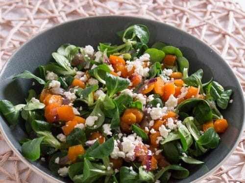 Eine Schale Feldsalat mit Möhren, zerbröckeltem Feta und roten Zwiebeln auf einem hellen Tisch - perfekt für einen Wintersalat.