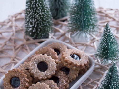 Ein Teller mit schokoladengefüllten und mit Puderzucker bestäubten Linzer Tortenplätzchen.