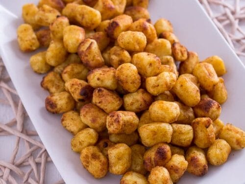Ein rechteckiger weißer Teller, gefüllt mit goldbraunen, knusprigen Gnocchi aus der Heißluftfritteuse.