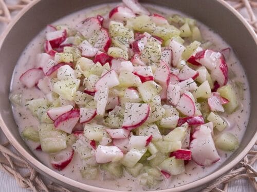 Eine Schale mit cremigem Gurken-Radieschen-Salat, garniert mit Dill.