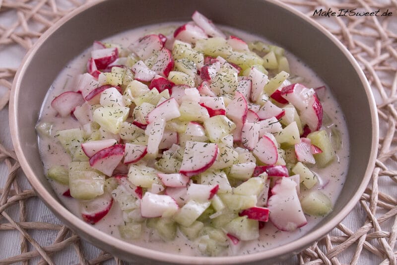 Eine Schüssel mit einem Gurken-Radieschen-Salat in einem Joghurt-Dressing. Darüber ist Dill gestreut.