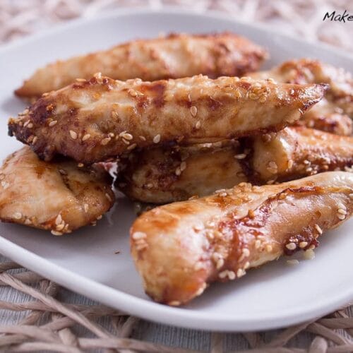 Sesamüberzogenes Hähncheninnenbrustfilet aus der Heißluftfritteuse auf einem weißen quadratischen Teller.