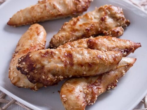 Ein weißer Teller mit mehreren Stücken gekochtem, glasiertem Hähncheninnenbrustfilet aus der Heißluftfritteuse, auf einem Platzset.