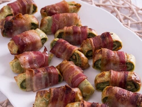 Auf einem weißen Teller liegen mehrere mit Bacon umwickelte Maultaschen Stücke.