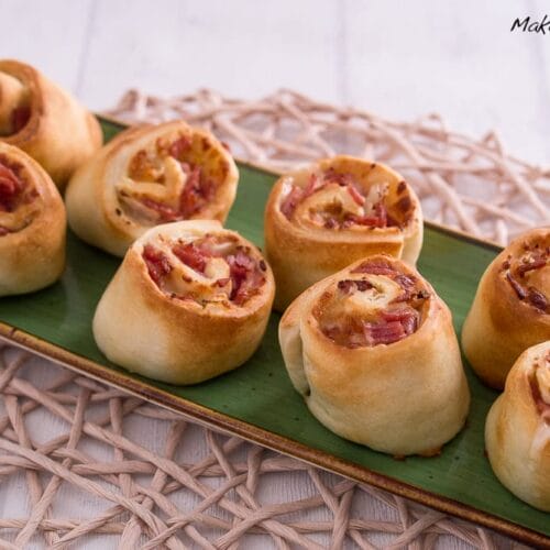 Pizzaschnecken aus der Heißluftfritteuse mit Salami und Schinken 3 Pizzaschnecken mit Salami, Schinken und Käse auf einem grünen, rechteckigen Teller.