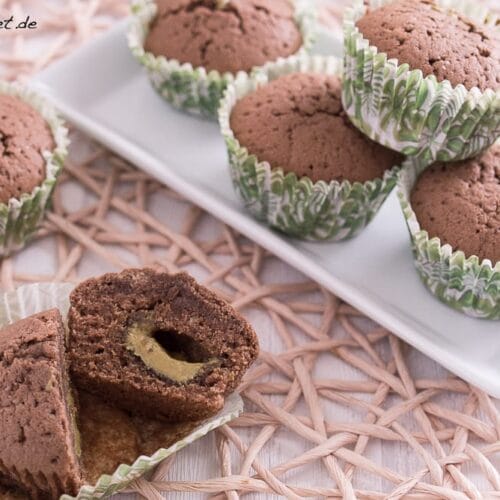 Schokomuffins mit Pistaziencreme Füllung 3 Schokoladenmuffins in grüner Verpackung, von denen einer aufgeschnitten wird, um eine Pistaziencreme Füllung zu enthüllen.