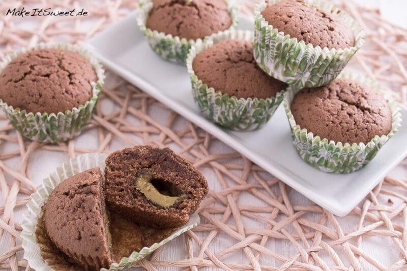 Mehrere Schokomuffins auf einem Teller. Davor ist ein Muffin aufgeschnitten, in der Mitte ist eine Pistaziencreme Füllung.