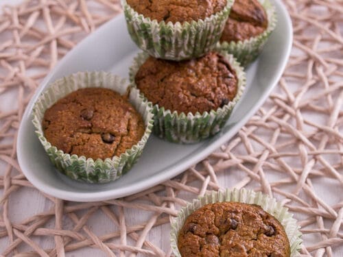Fünf Haselnuss-Joghurt-Muffins in grünen Pappbechern auf einem weißen Teller, wobei ein Muffin an der Spitze steht.
