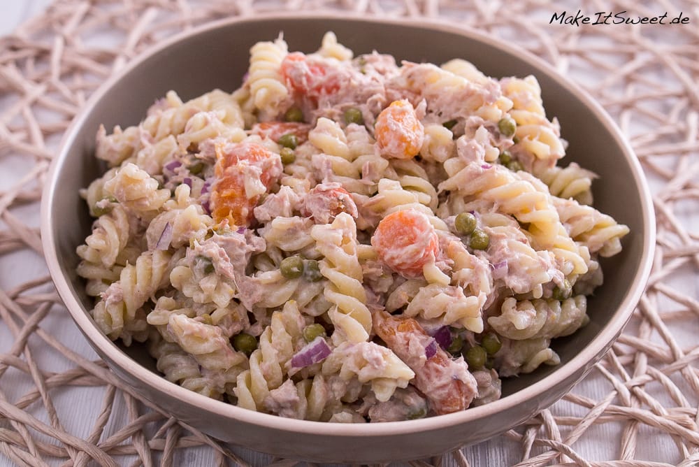 Schüssel mit cremigem Nudelsalat mit Thunfisch, Erbsen, Karotten und roten Zwiebeln.