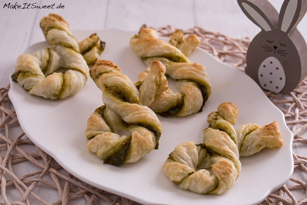 Gedrehte Blätterteig-Hasen aus Blätterteig mit Pesto auf einem weißen Teller angerichtet.