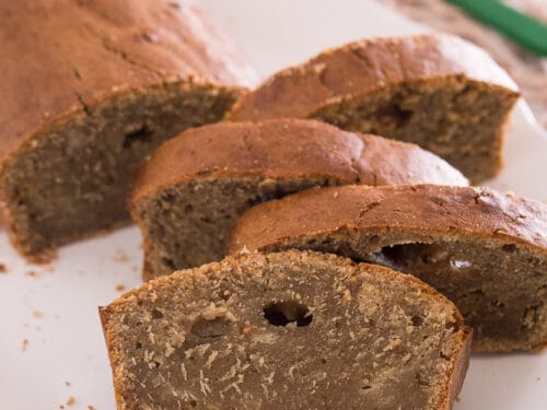 In Scheiben geschnittenes braunes Bananenbrot mit Erdnussmus auf einem weißen Teller.