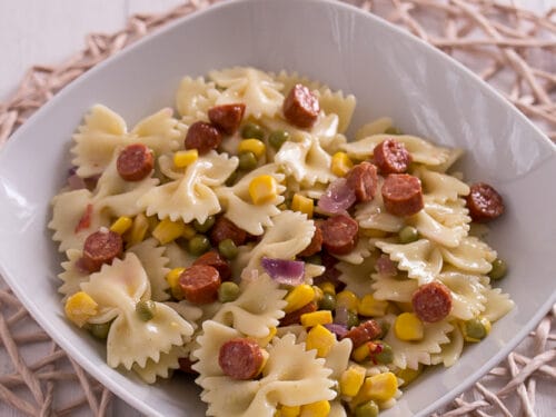 Schüssel mit Farfalle-Nudelsalat mit Mais, Erbsen, roten Zwiebeln und Wurst in Scheiben (Kabanossi).