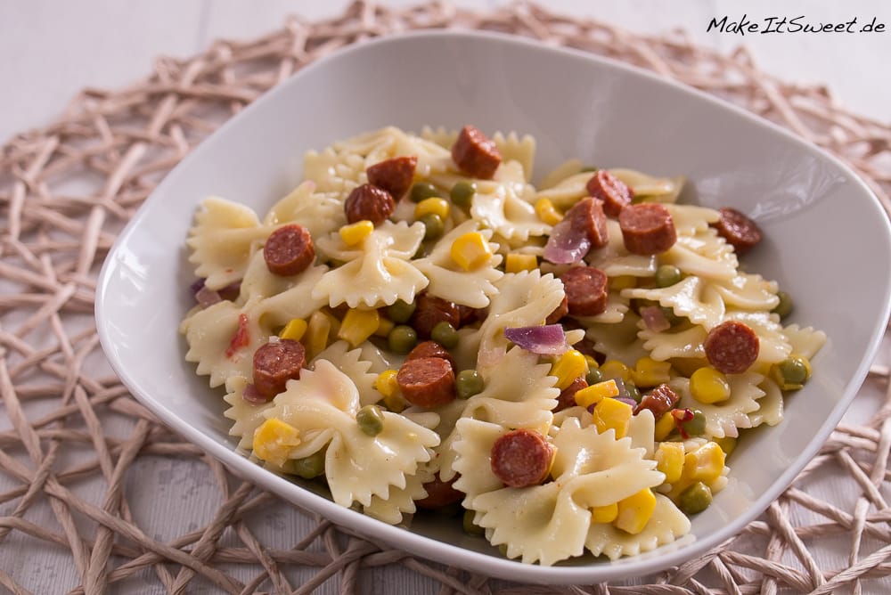 Schüssel mit Schleifen-Nudelsalat mit Mais, Erbsen, roten Zwiebeln und Kabanossi-Wurst.