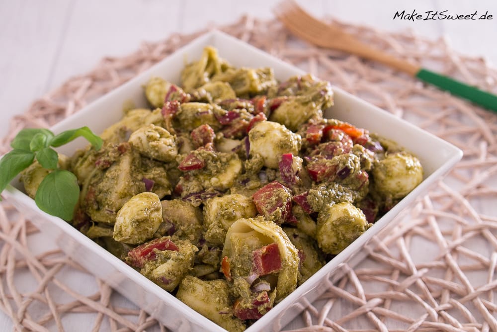 Quadratische Schüssel mit Tortellini-Salat mit Pesto, roten Zwiebeln und Paprika.