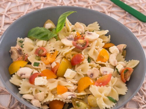 Schüssel mit Farfalle-Nudelsalat mit Tomaten, Pilzen, Feta und Basilikum.