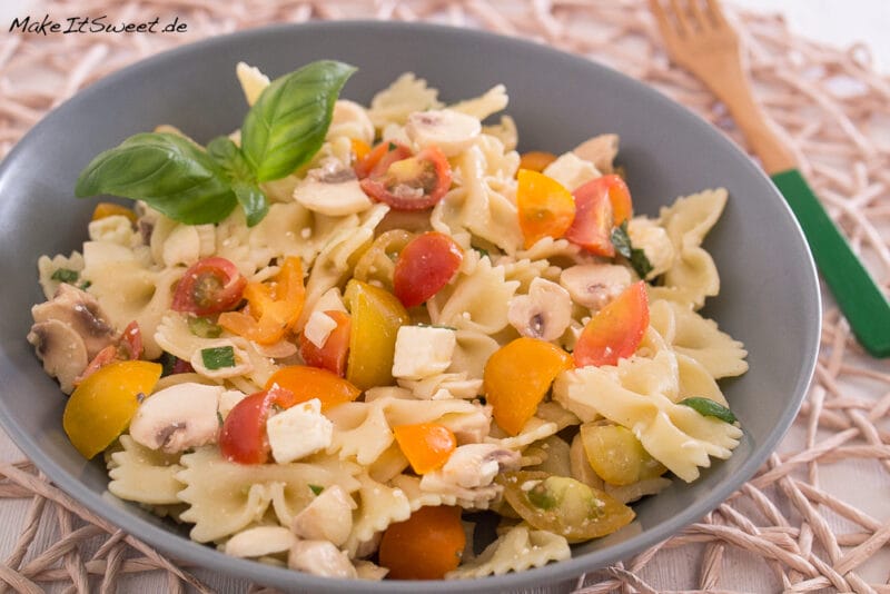 Eine Schüssel mit Nudelsalat mit Tomaten, Champignons und Feta sowie Basilikum.