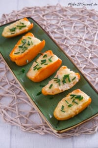 Sechs gebackene Mini-Paprikahälften mit geschmolzenem Käse und gehacktem Schnittlauch.