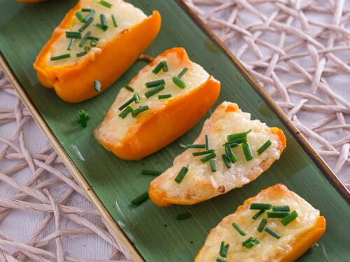 Sechs gebackene Mini-Paprikahälften mit geschmolzenem Käse und gehacktem Schnittlauch.