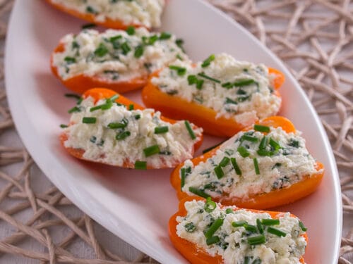 Mini-Paprika gefüllt mit einer Feta-Creme, bestreut mit Schnittlauch auf weißem Teller.