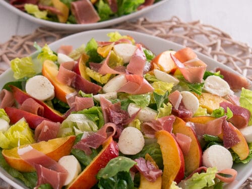 Zwei Teller Nektarinen-Mozzarella-Salat mit Pfirsichspalten, Mozzarellakugeln, Prosciutto und knackigem Salat.