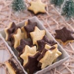 Plätzchen mit Erdnussbutter Füllung Eine rechteckige Schale, gefüllt mit sternförmigen Keksen, einige aus Natur und einige aus Schokolade, steht auf einem gewebten Tischset neben kleinen dekorativen Tannenbäumen.