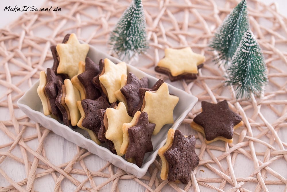 Sternförmige Vanille- und Schokoladenkekse mit einer Füllung aus Erdnussbutter, die in einer Schale angeordnet sind.