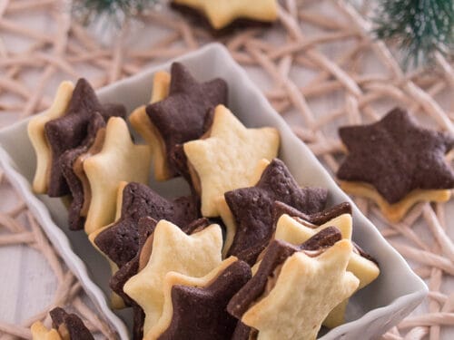 Sternförmige Kekse aus Schokolade und Vanille mit Erdnussbutter Füllung, in einer weißen Schale.
