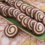 Auf einem rechteckigen grünen Teller liegt eine Reihe von Schwarz-Weiß-Gebäck, ein klassisches deutsches Gebäck mit Schokoladen- und Vanillekipferln, fein säuberlich angeordnet. Der Teller steht auf einem geflochtenen Tischset mit dekorativen goldenen Sternen in der Nähe.