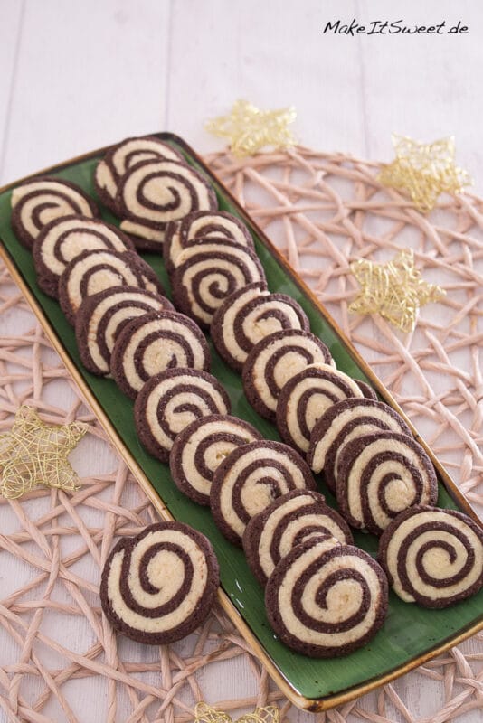 Auf einem rechteckigen grünen Teller liegen Reihen von Schwarz-Weiß-Gebäck Plätzchen.