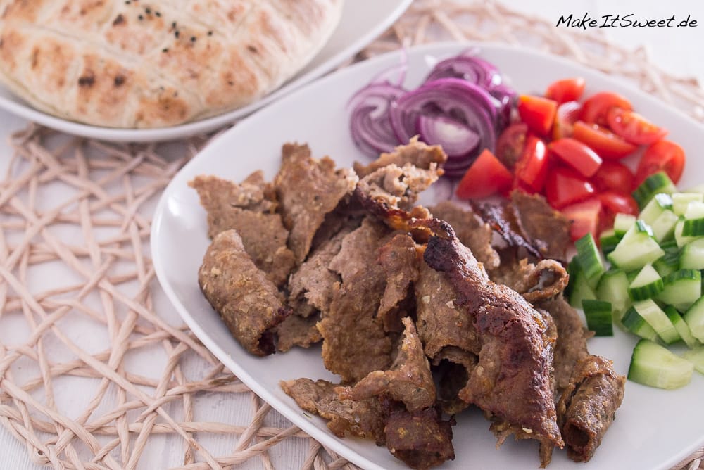 Mit Backpapier-Dönerfleisch, geschnittenen roten Zwiebeln, Tomaten, Gurken und Fladenbrot anrichten.