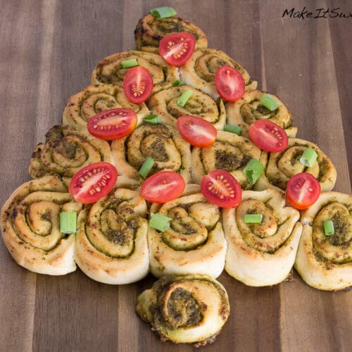 Pesto Tannenbaum - herzhaftes Fingerfood Weihnachten 4 Pesto-Tannenbaum-Rollen in Form eines Weihnachtsbaums, belegt mit Kirschtomaten und grünen Zwiebeln auf einem Holzbrett.
