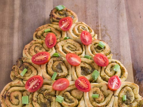 Tannenbaum Pesto-Brötchen mit Kirschtomaten und Frühlingszwiebeln auf einem Holzbrett angerichtet.