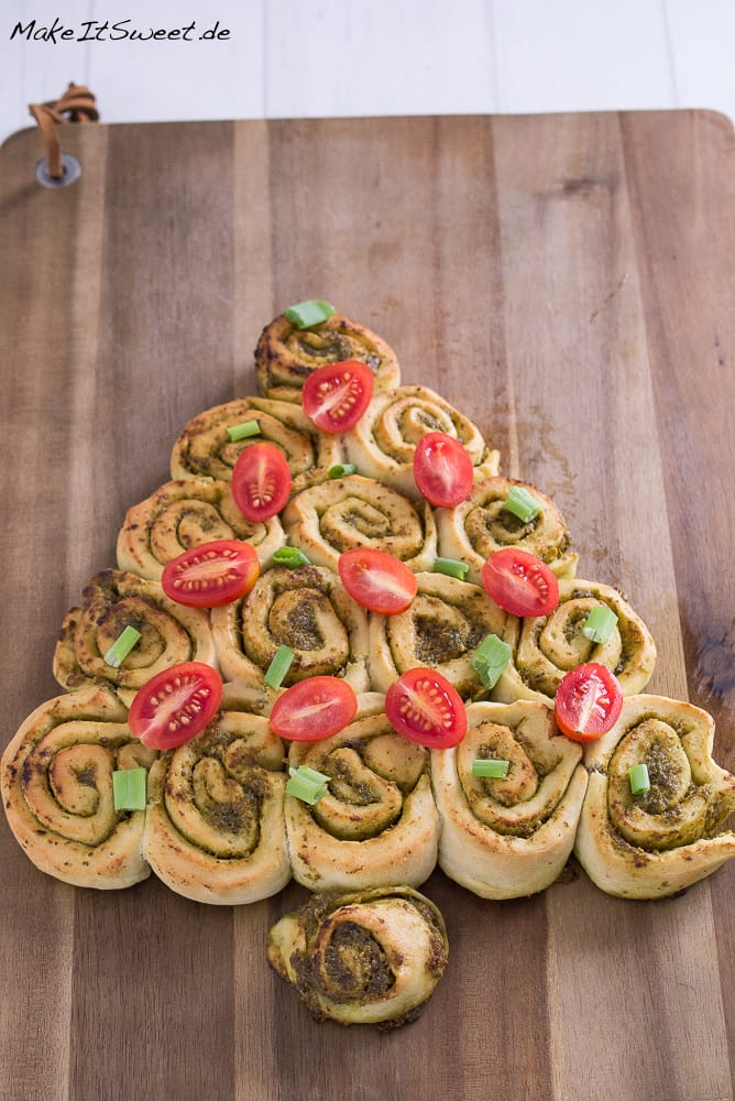 Pesto Tannenbaum - herzhaftes Fingerfood Weihnachten 4 Ein weihnachtlicher Pesto-Tannenbaum aus herzhaften Pinwheel-Rollen auf einem hölzernen Schneidebrett, dekoriert mit halbierten Kirschtomaten und gehackten grünen Zwiebeln - perfektes Fingerfood Weihnachten für Ihren Festtagstisch.