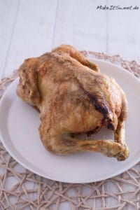 Ganzes gefülltes Hähnchen in der Heißluftfritteuse mit Maronen, Apfel und Zwiebeln 3 Ganzes gefülltes Hähnchen, goldbraun aus der Heißluftfritteuse, serviert auf einem weißen Teller.