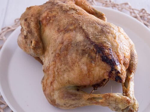 Ganzes gefülltes Hähnchen, goldbraun aus der Heißluftfritteuse, serviert auf einem weißen Teller.